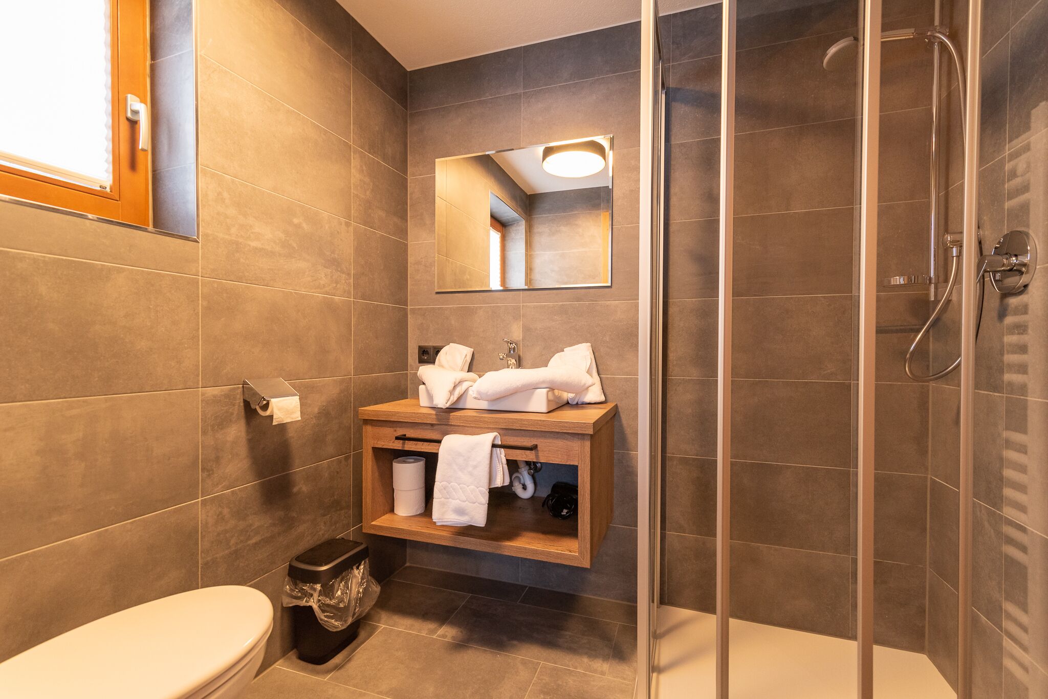Un baño moderno con cabina de ducha de vidrio, un tocador de madera con espejo y un inodoro.