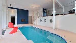 An indoor swimming pool with a modern design, a staircase with a glass railing, and a bright color scheme.