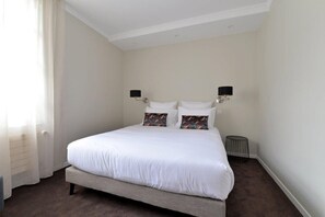 A hotel room with a large bed, two wall-mounted lamps, a small round table, and a radiator. - Satin Take advantage of this comfortable and refined apartment for 2 people. (Masevaux)