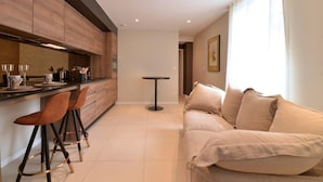 A modern kitchen with wooden cabinets, a bar area with stools, a round table, and a beige sofa.