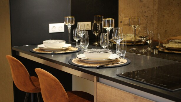 A modern dining area with a long table set for two, featuring white plates, clear glasses, and a central decorative bowl.