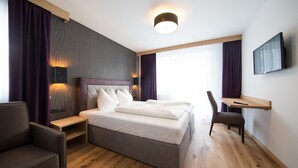Una habitación de hotel moderna con una cama grande, un escritorio, una silla y un televisor montado en la pared.