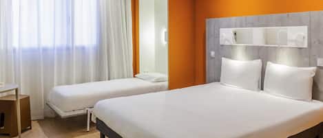 A hotel room with two beds, a desk, and a mirror.