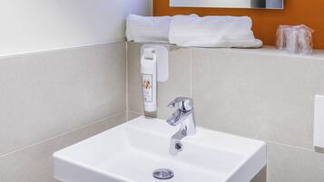 A modern bathroom with a white sink, chrome faucet, and a towel dispenser.