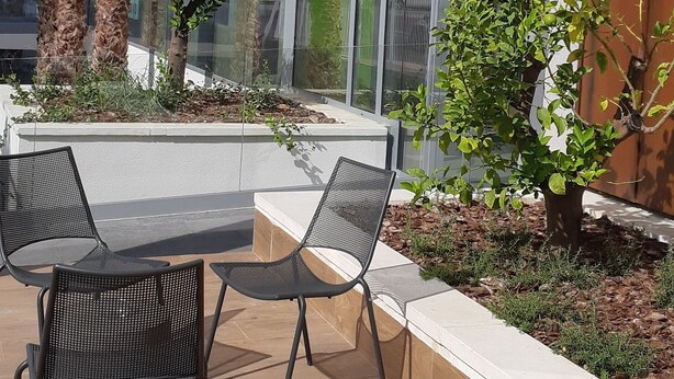 Un edificio moderno con un letrero que dice “ibis budget” y un patio con mobiliario exterior y plantas.