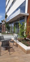 Un edificio moderno con un letrero que dice “ibis budget” y un patio con mobiliario exterior y plantas.