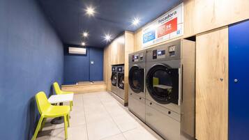 A laundry room with three washing machines, a bench, and a table with chairs.