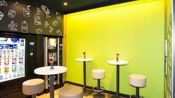 Un interior moderno con una máquina expendedora, tres taburetes y una pared de color verde brillante.