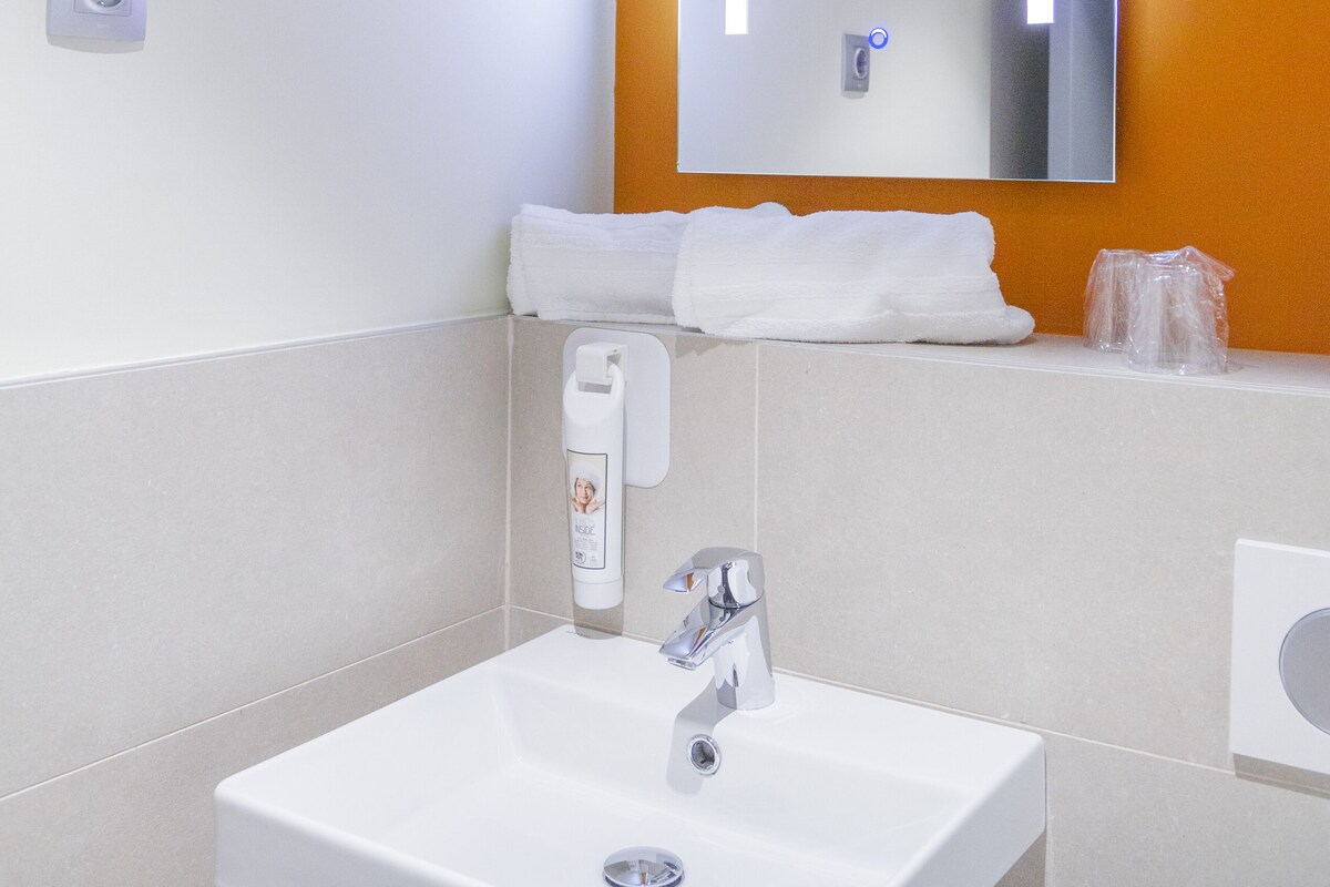 Un baño con un lavamanos blanco, un espejo y una pared de acento naranja.