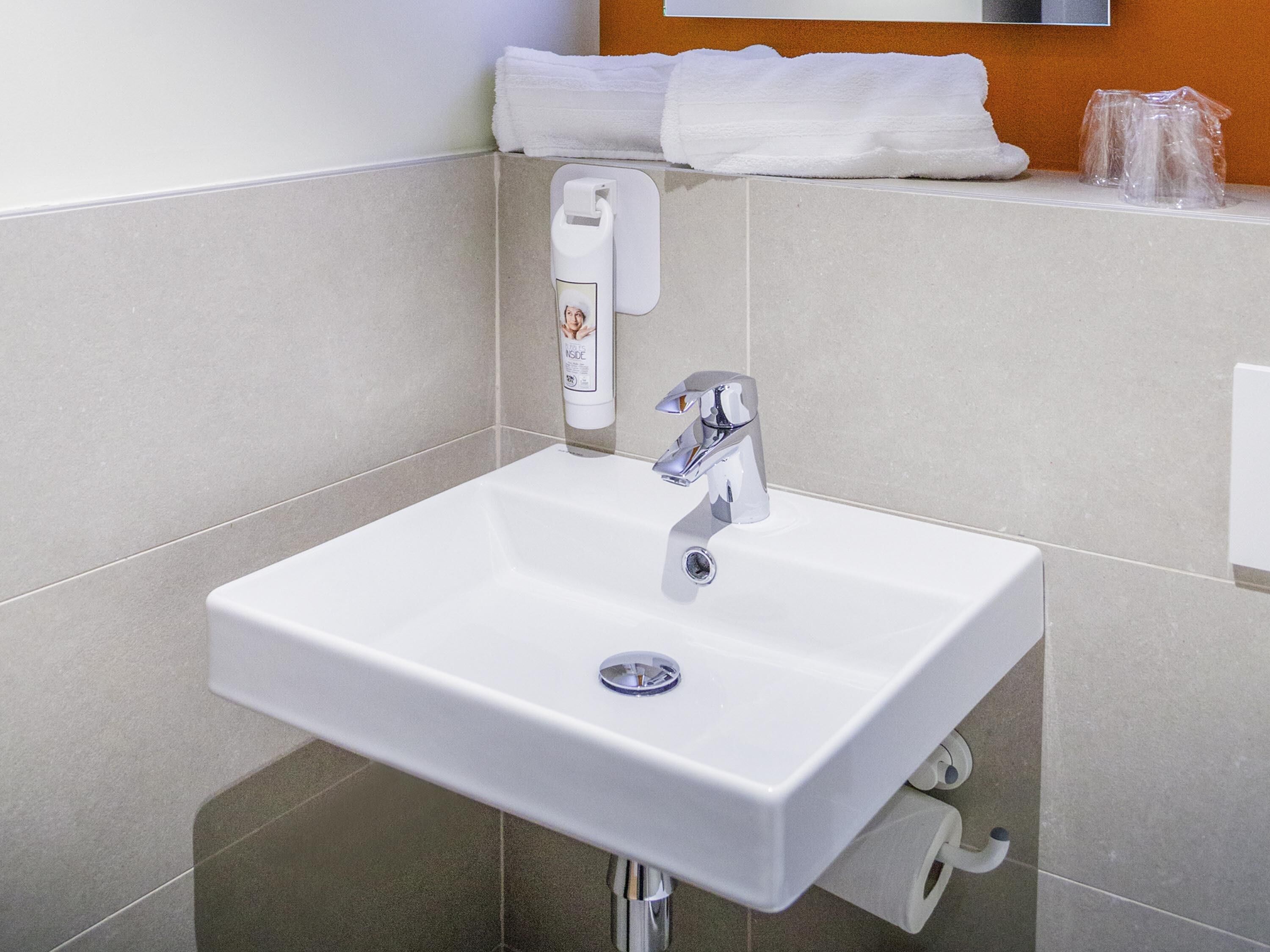 Un baño con un lavamanos blanco, grifo cromado y dispensador de jabón.