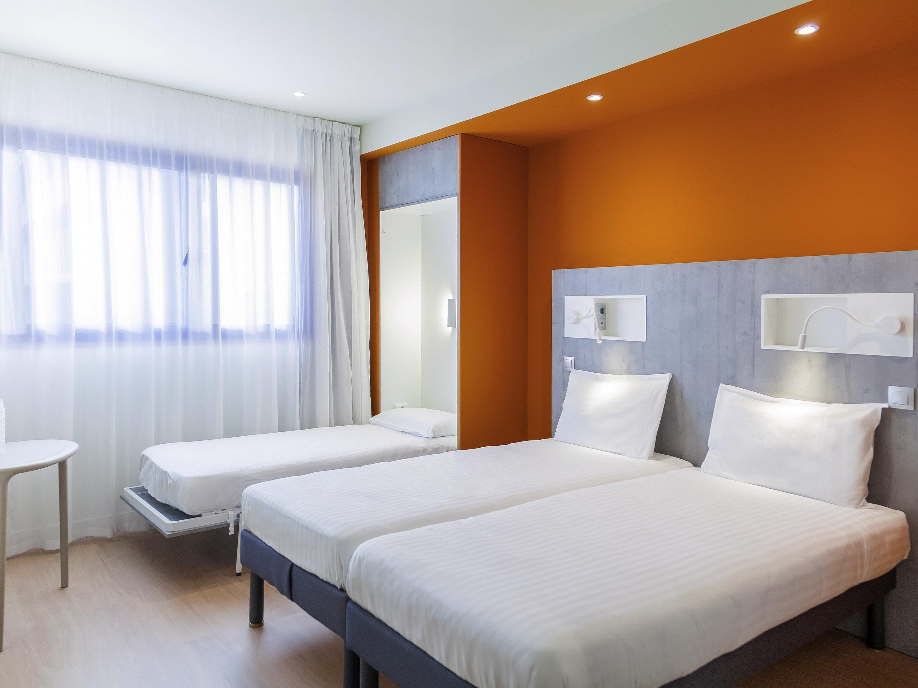 Ein Hotelzimmer mit zwei Betten, einem kleinen Tisch, einem Spiegel und einer Duschkabine.