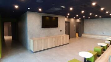 A modern interior with a reception desk, seating area, and a flat-screen TV mounted on the wall.