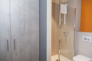 Un baño con ducha de vidrio, inodoro blanco y un mueble con dos pomos.