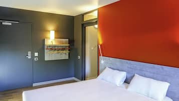 Una habitación de hotel moderna con una cama grande, un perchero de toallas en la pared y una puerta que da a otra habitación.