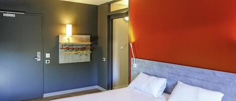 Una habitación de hotel moderna con una cama grande, un perchero de toallas en la pared y una puerta que da a otra habitación.