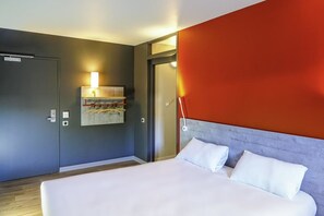 Una habitación de hotel moderna con una cama grande, un perchero de toallas en la pared y una puerta que da a otra habitación.