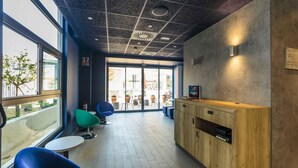 Un área de recepción moderna con un mostrador de madera, sillas azules y una puerta de vidrio que da al exterior.