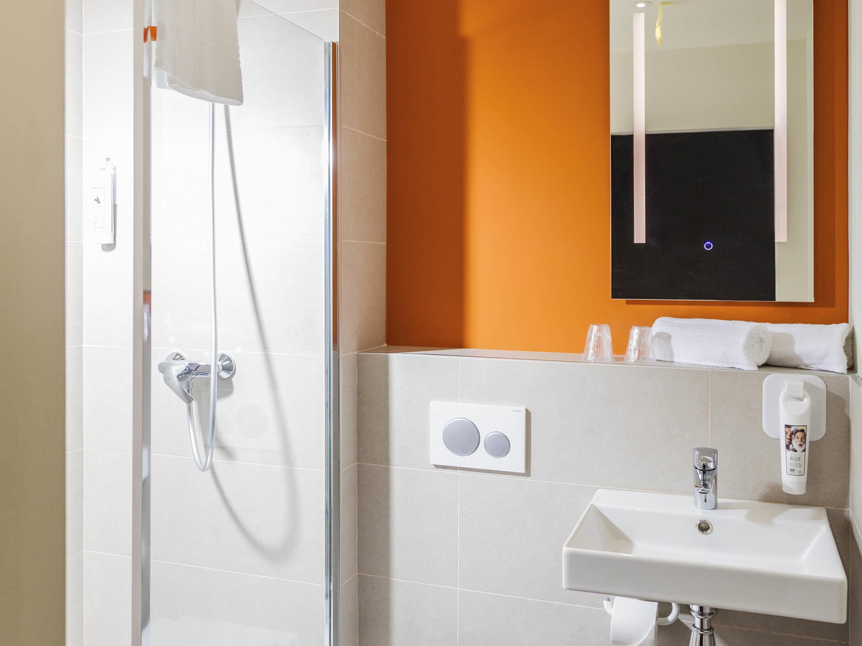Un baño moderno con cabina de ducha de vidrio, un lavabo blanco y un espejo encima.