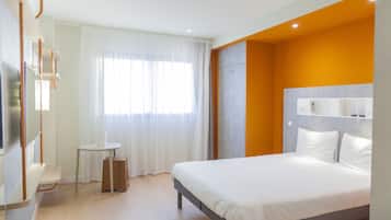 Une chambre d’hôtel moderne, équipée d’un lit, d’une petite table et d’une fenêtre avec des rideaux.