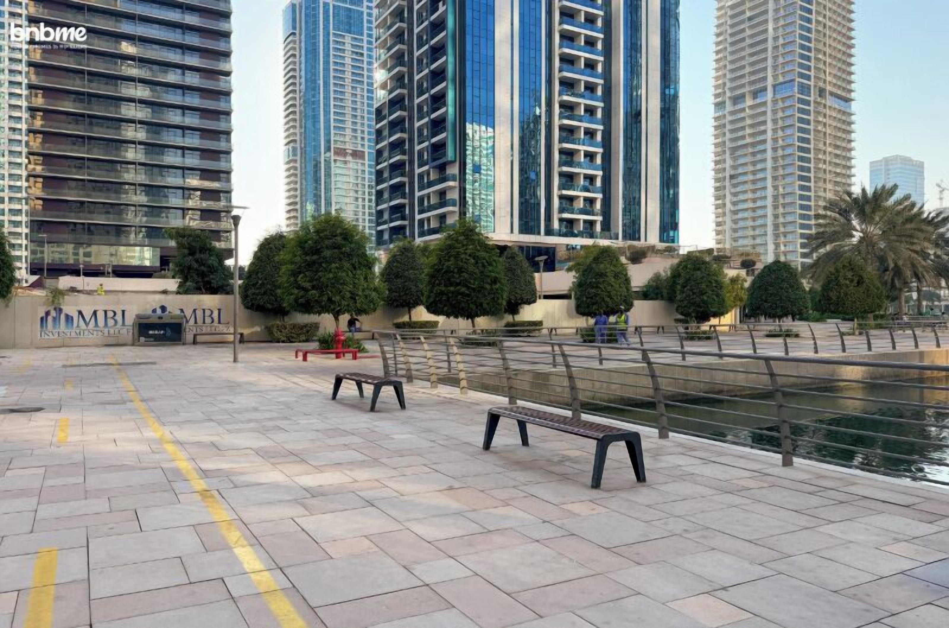 Una piazza moderna in città, con panchine, una fontana e alti edifici sullo sfondo.