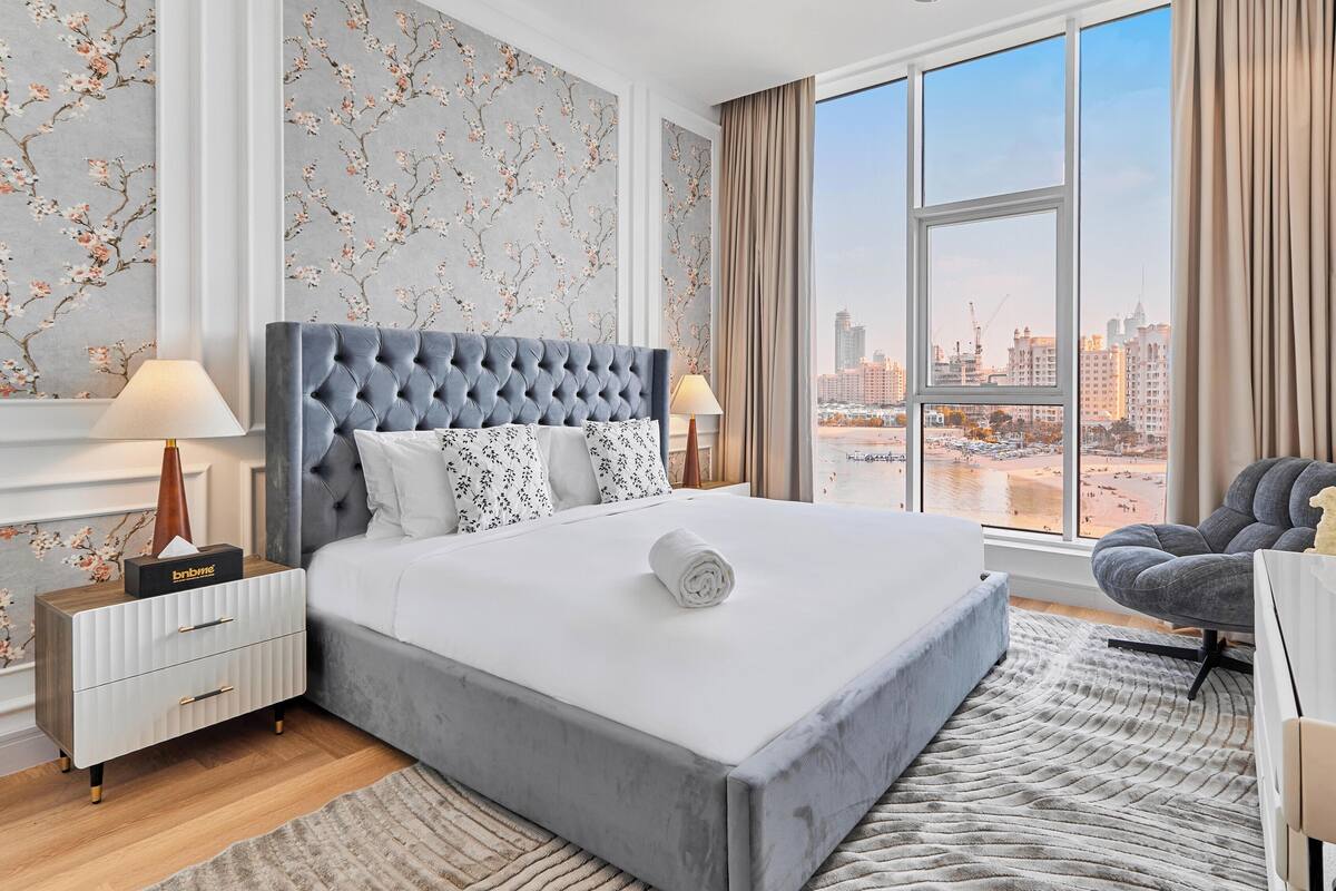 Une chambre d’hôtel moderne dotée d’un grand lit, d’un bureau, d’une chaise, d’une grande fenêtre donnant sur la ville et d’un miroir décoratif.