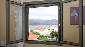 A room with a window open, revealing a view of buildings and hills. - Charming Apartment in Kefalonia Island (Kefalonia)