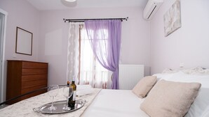 A bedroom with a bed, bedside table, and a window with purple curtains. - Charming Apartment in Kefalonia Island (Kefalonia)