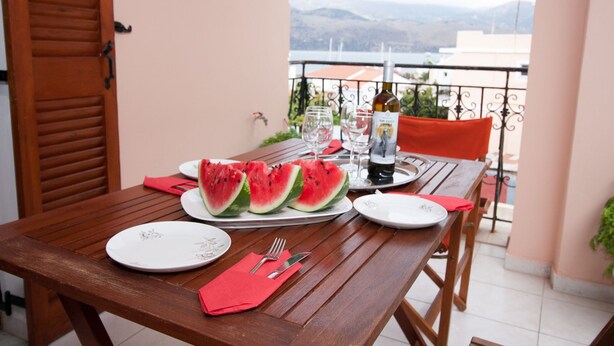 A wooden table set with plates, cutlery, a bottle, and glasses, with a view of mountains in the background. - Charming Apartment in Kefalonia Island (Kefalonia)