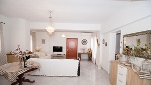 A well-lit bedroom with a bed, bedside table, and a dresser. A television is mounted on the wall, and there is a door leading to another room. - Charming Apartment in Kefalonia Island (Kefalonia)