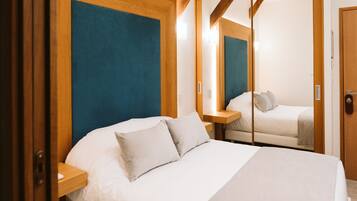 Quarto de hotel moderno com cama grande, cabeceira de madeira e um espelho refletindo o quarto.