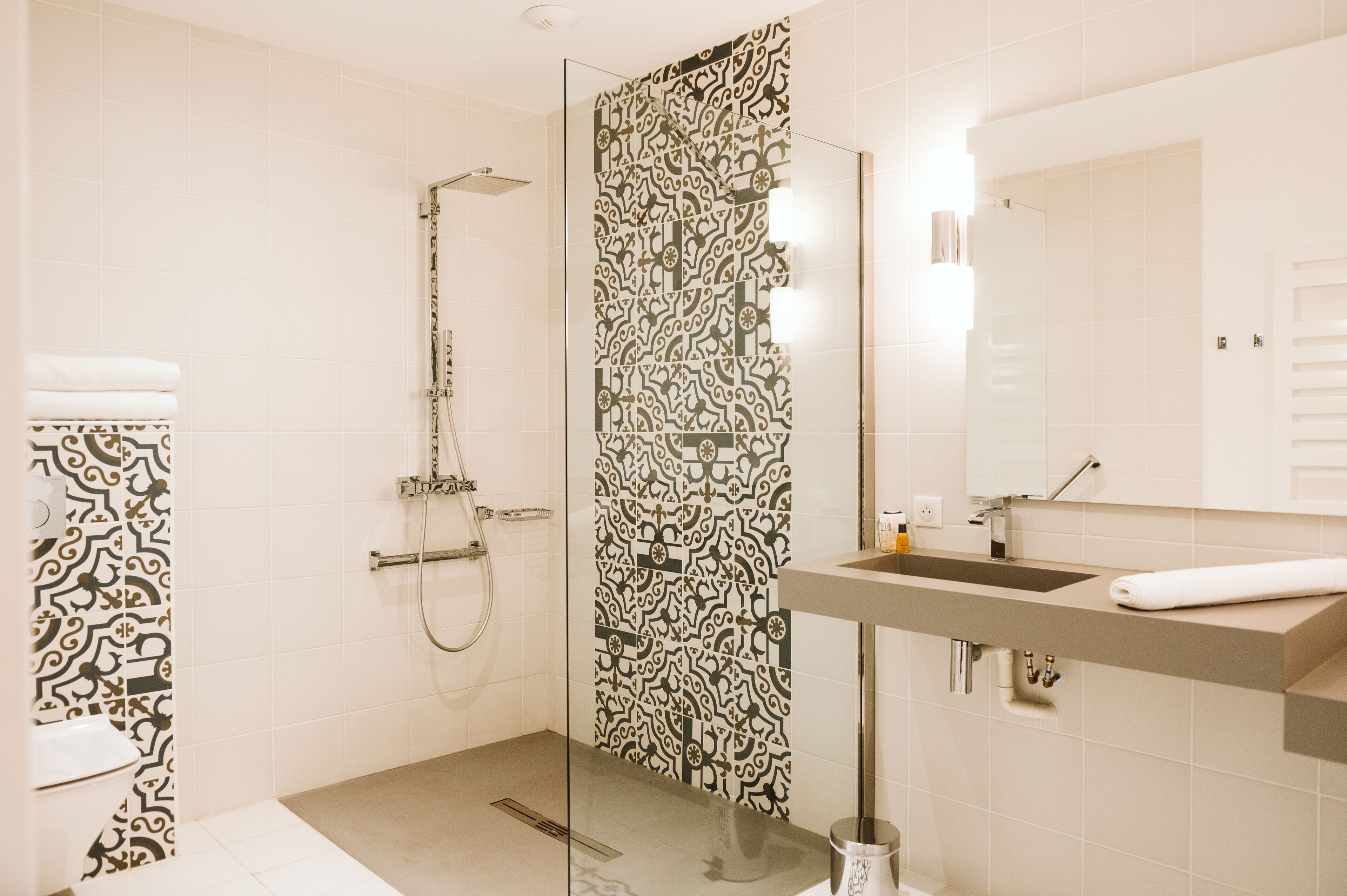 Un baño moderno con cabina de ducha de vidrio, pared con azulejos estampados y lavamanos con toalla.
