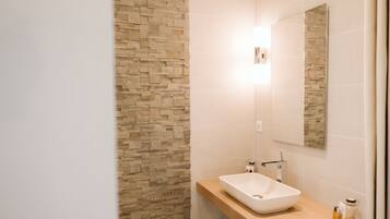 Une salle de bain moderne avec un mur en pierre, un lavabo blanc et un miroir.