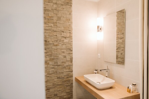 A modern bathroom with a stone wall, a white sink, and a mirror. - Domaine d'en Fargou (Saint-Sulpice)