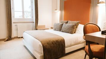 A neatly made bed with a brown throw blanket, a wooden nightstand, a chair, and a window with curtains.