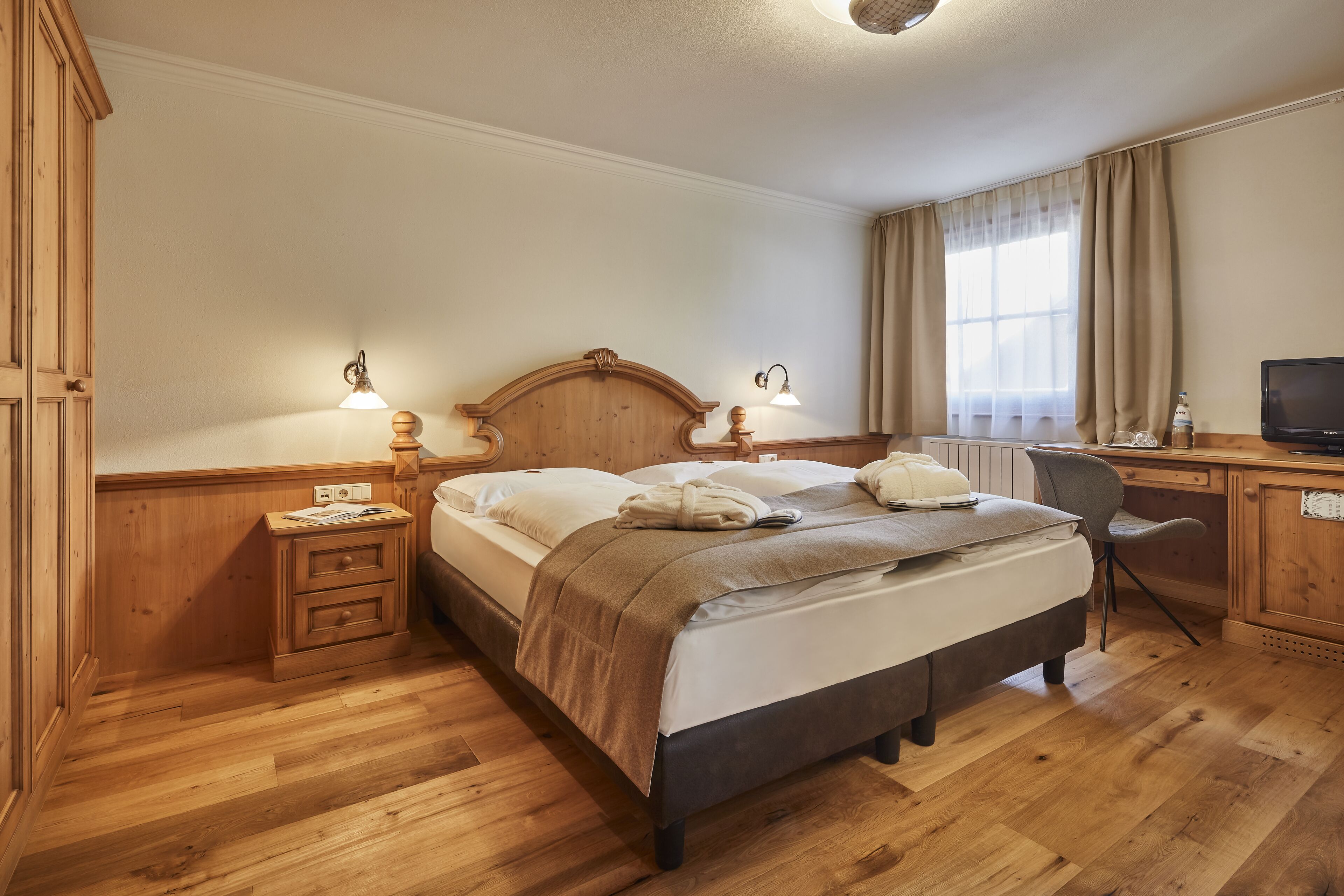 Een netjes ingerichte slaapkamer met een houten bed, nachtkastjes, een bureau en een televisie.