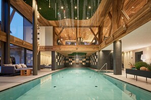 Ein Hallenbad mit Holzbalken, einer Sitzecke mit Sofas und Blick auf den Himmel durch große Fenster.