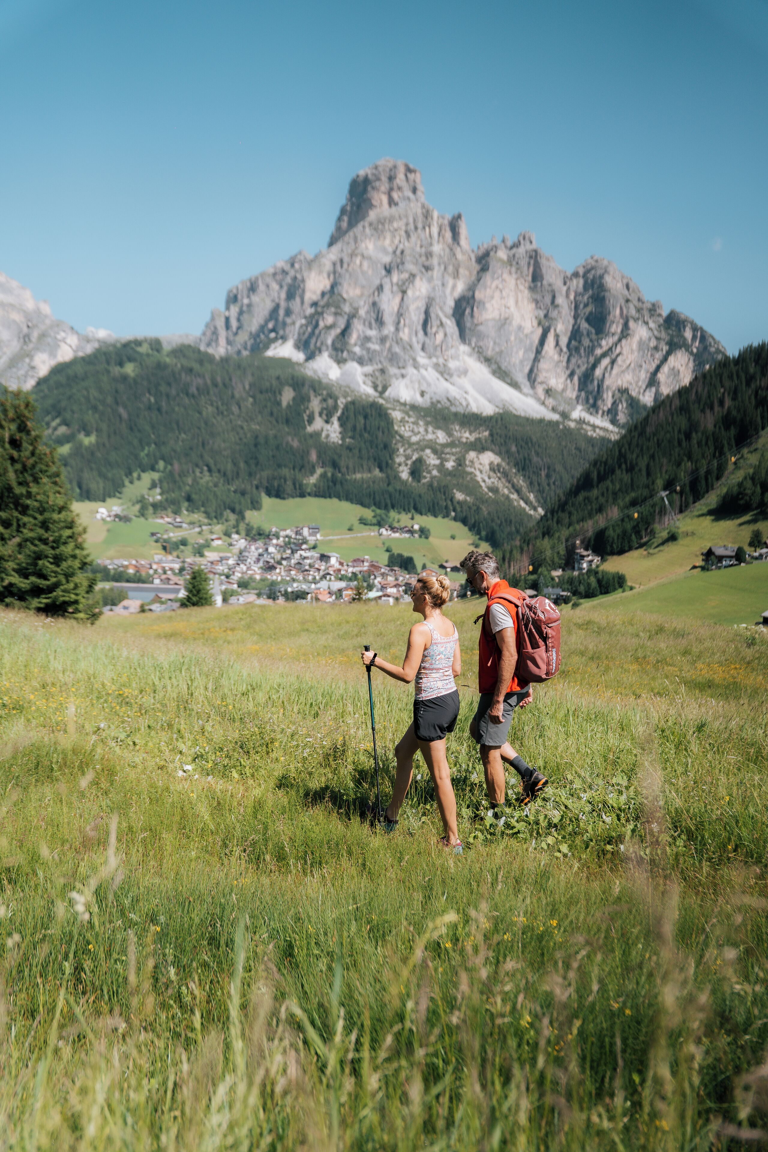 A couple hiking in a grassy field with a mountain range in the background.