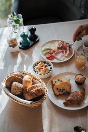 Ein Frühstückstisch mit verschiedenen Speisen, darunter Brot, Gebäck und ein Glas Orangensaft.