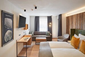 Ein Hotelzimmer mit Bett, Sofa, Schreibtisch, Sessel und Fernseher.