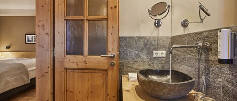 A wooden door with glass panels, a bathroom with a large stone sink, a mirror, a handheld showerhead, and a towel dispenser.