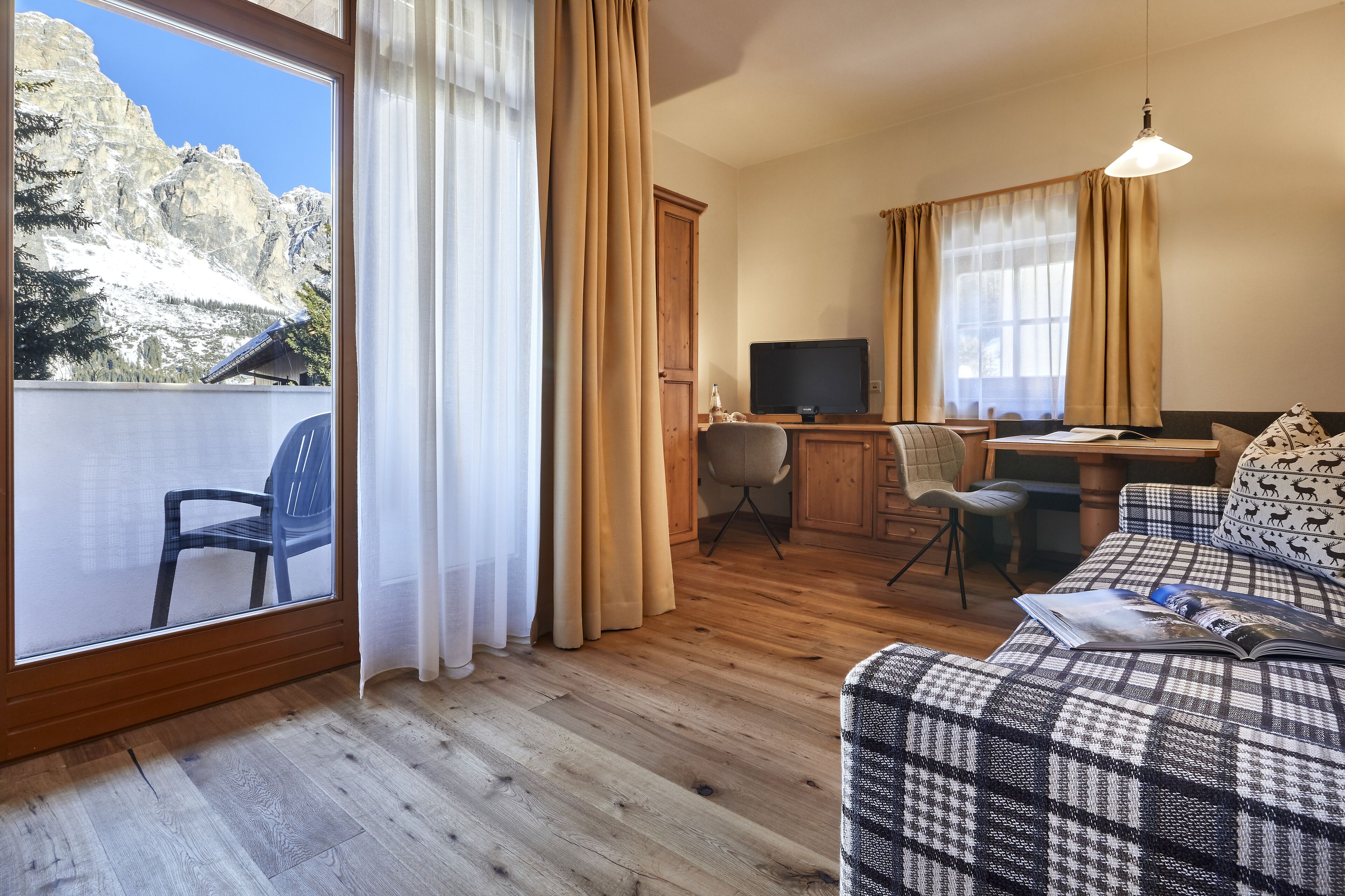Une pièce chaleureuse avec un plancher en bois, un canapé, un bureau avec une chaise, une télévision et une vue sur les montagnes par la fenêtre.