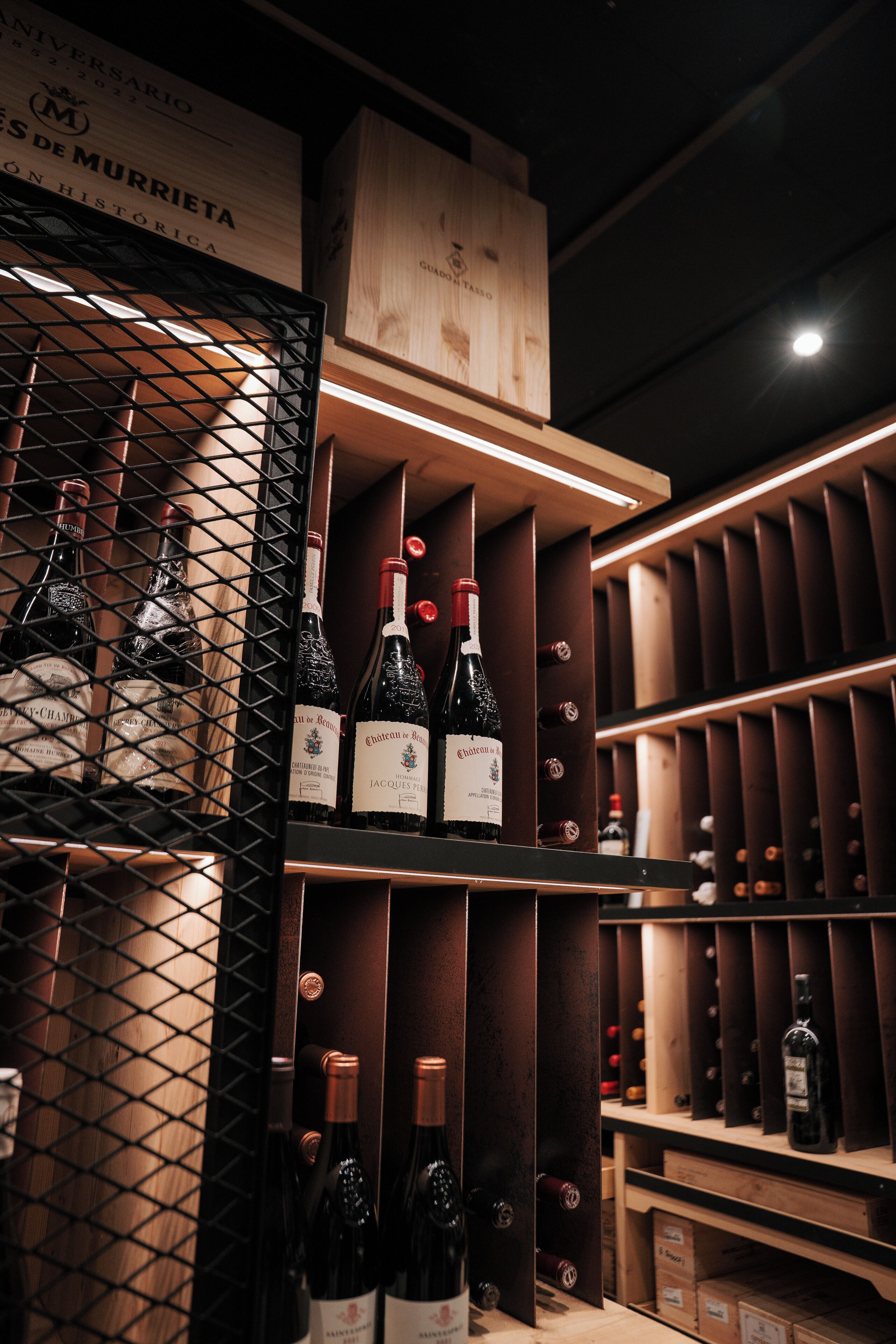 Una bodega con estantes de madera y cavas metálicas llenas de botellas de vino.