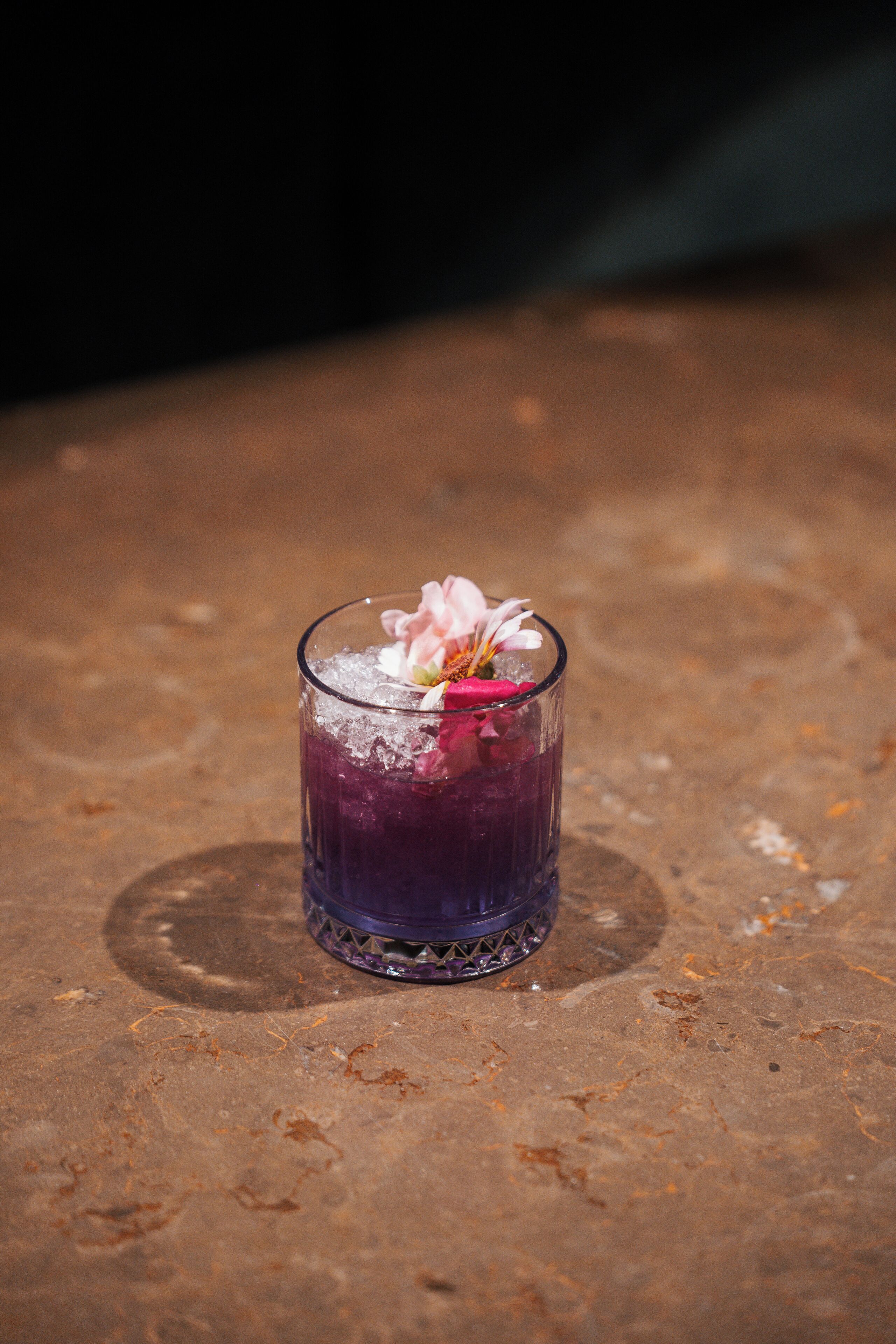 A glass of purple beverage with a flower on a textured surface.
