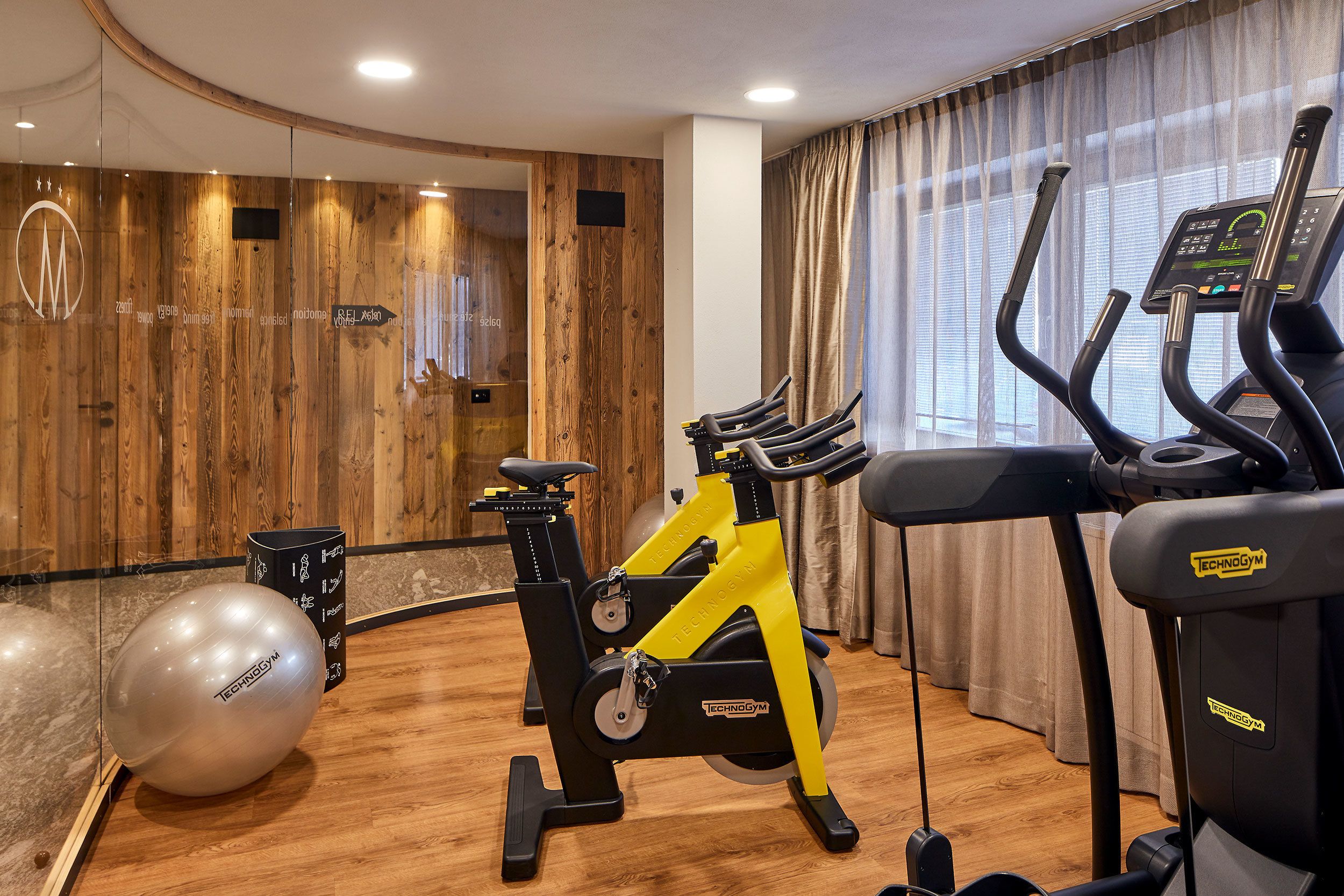 Un gimnasio con equipo de ejercicio, una pared de madera y una ventana con cortinas.