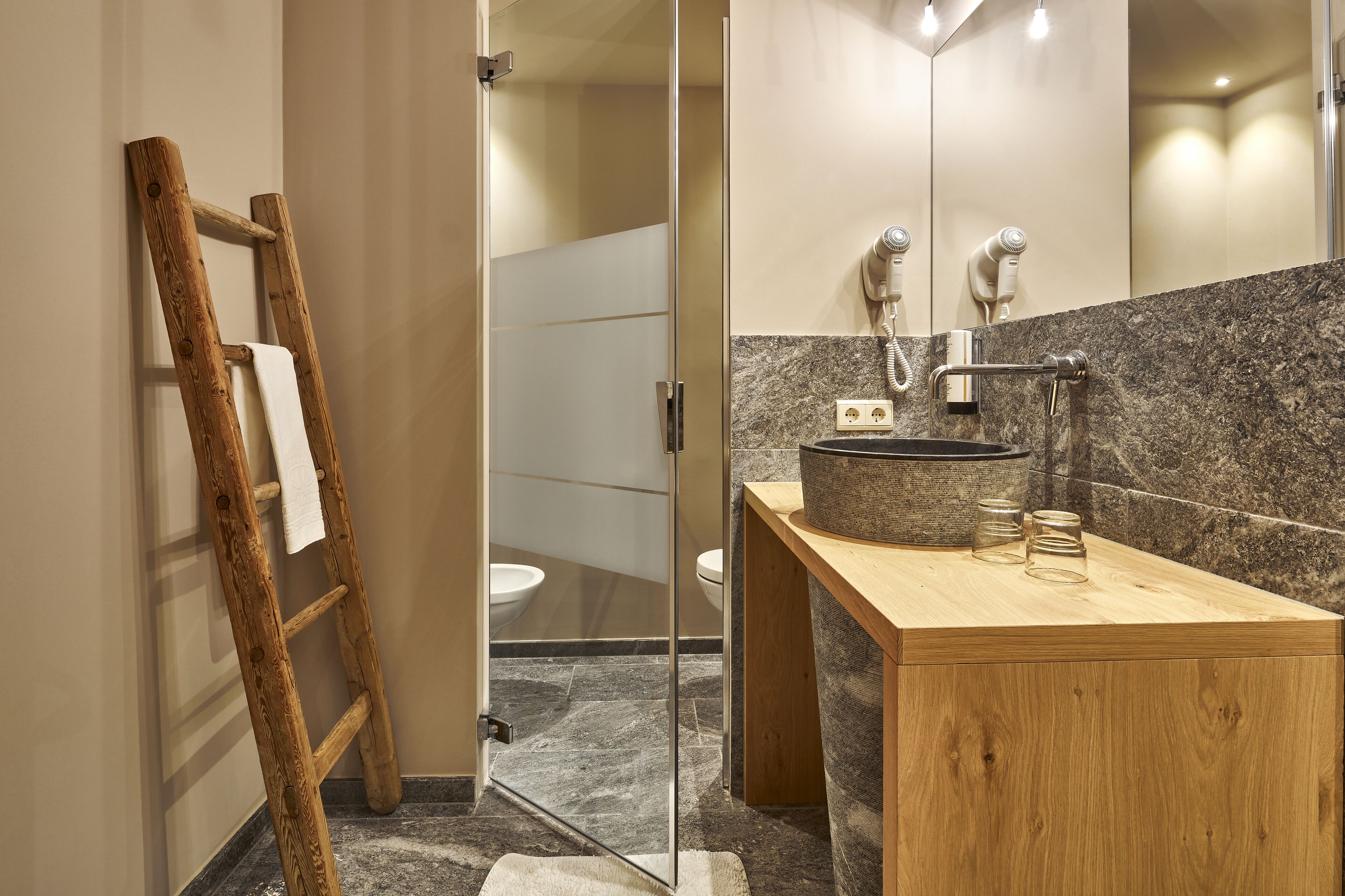 A modern bathroom with a wooden vanity, marble backsplash, and a glass shower enclosure.
