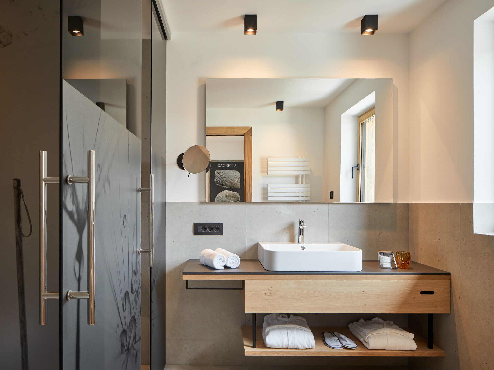 Un baño moderno con ducha de mármol, lavamanos blanco y tocador de madera.