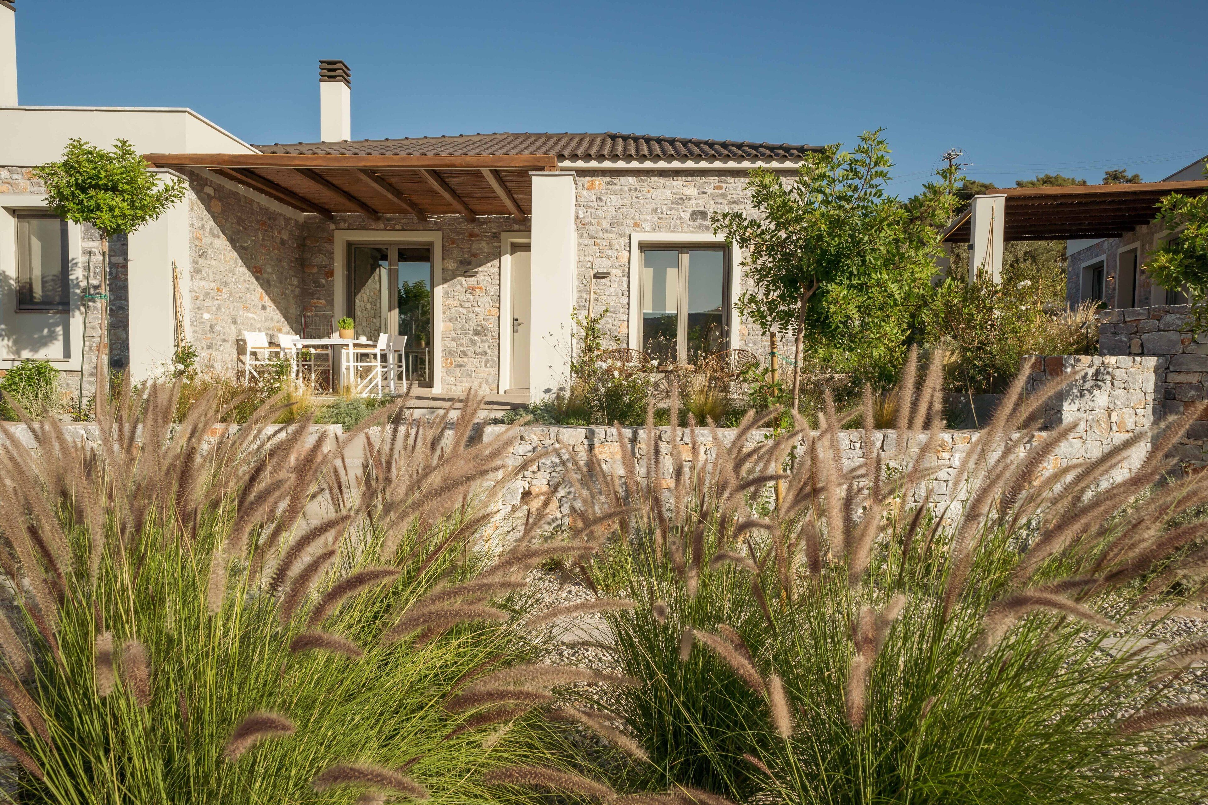 A modern house with stone walls, a wooden pergola, and a stone patio with outdoor furniture.