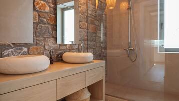 A modern bathroom with stone walls, a wooden vanity, two sinks, and a glass-enclosed shower area.