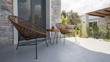 A patio with two wicker chairs and a small table, set against a stone wall and a glass door.