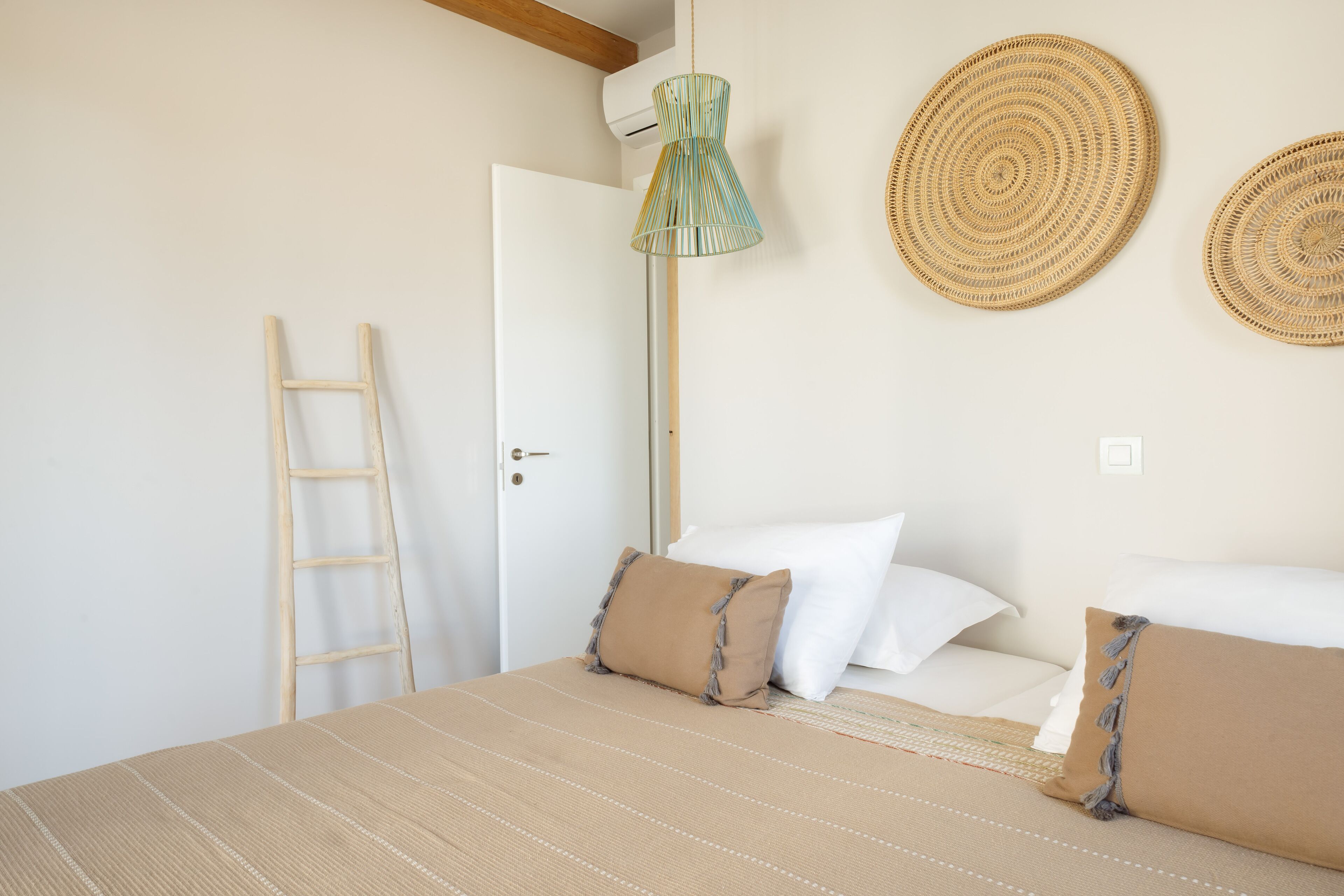A bedroom with a bed, pillows, a ladder, and two woven wall hangings.